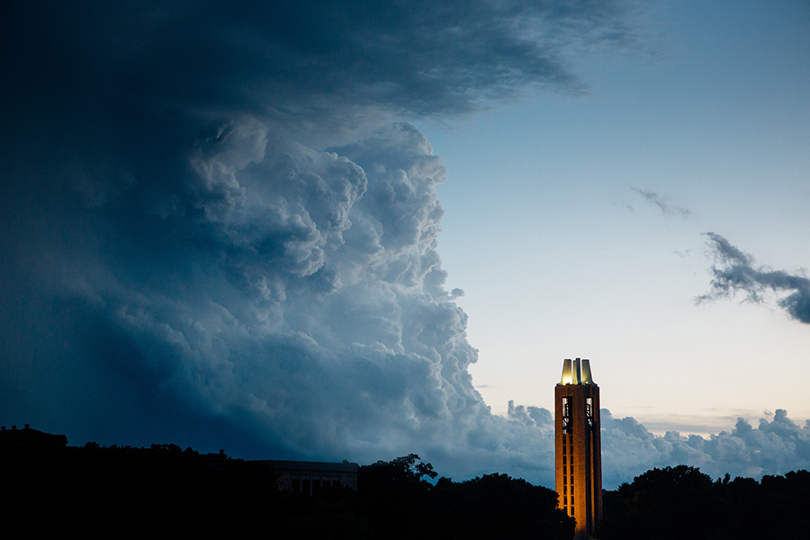 A large wall of storm clouds fill over half the shot with the Campanile tower and tree silhouettes shown in the lower third of the photo. 